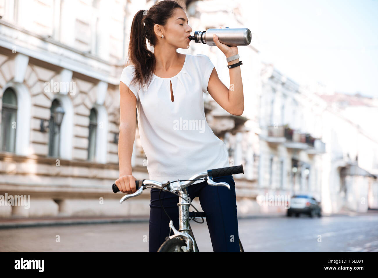 Young beautiful woman drinking water from the bottle while riding bicycle Stock Photo