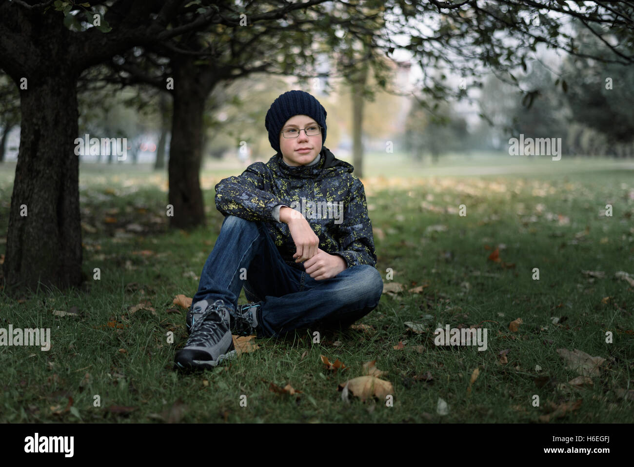 boy teenager in glasses sitting under a tree in autumn Stock Photo