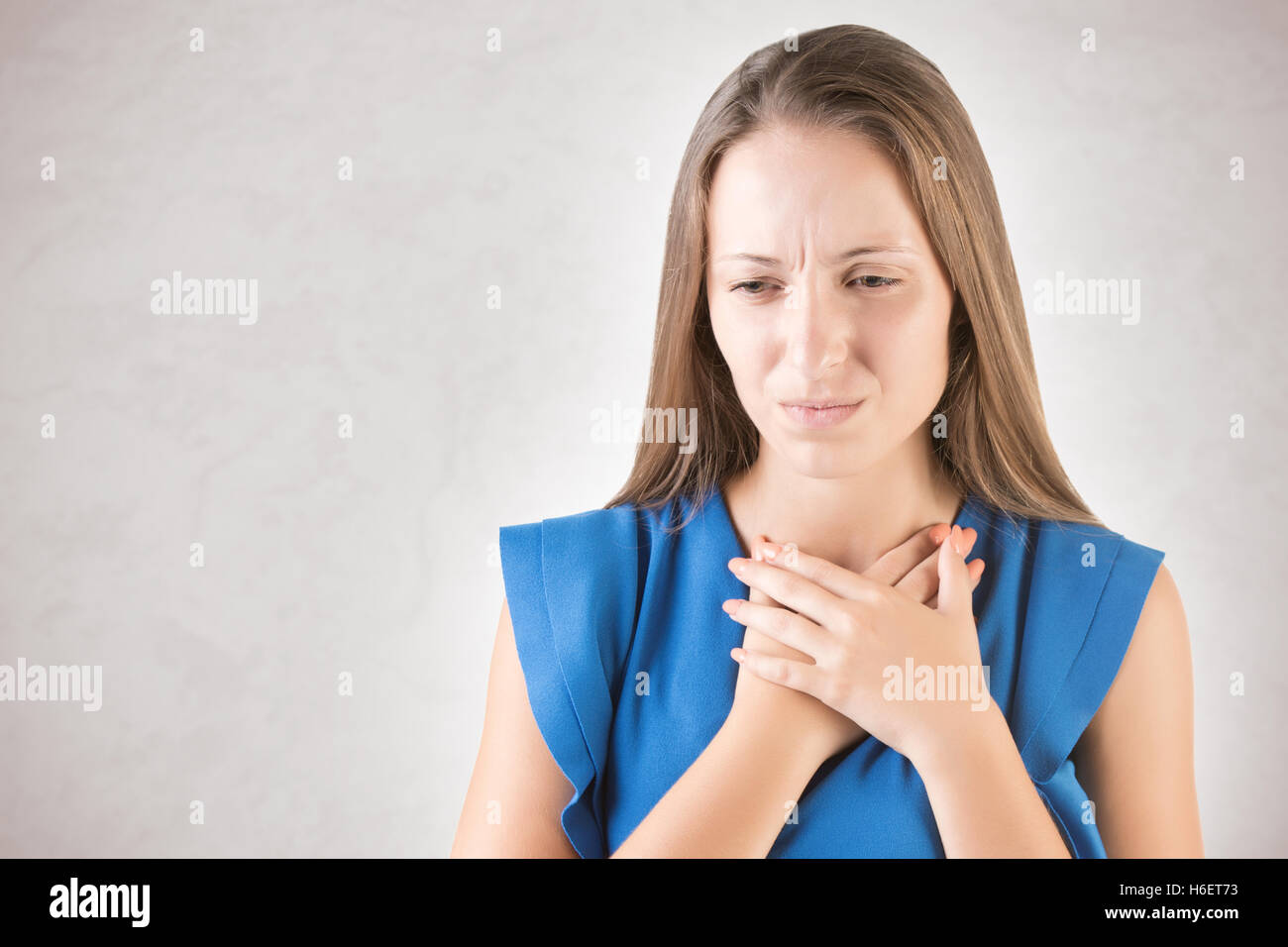 Woman with a sore throat holding her neck, isolated in grey Stock Photo