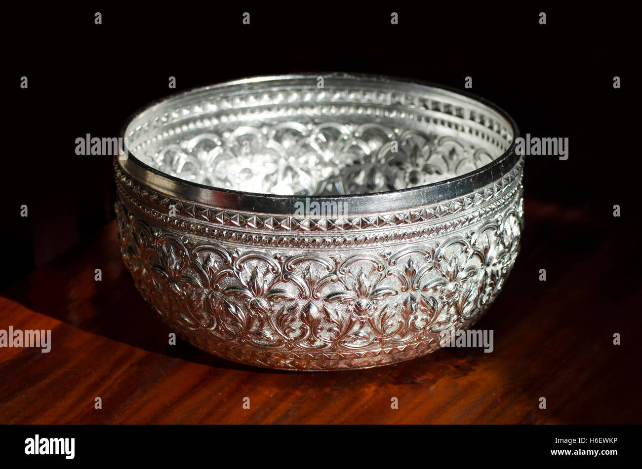 Silver bowl resting on wooden floor against a black background. Stock Photo