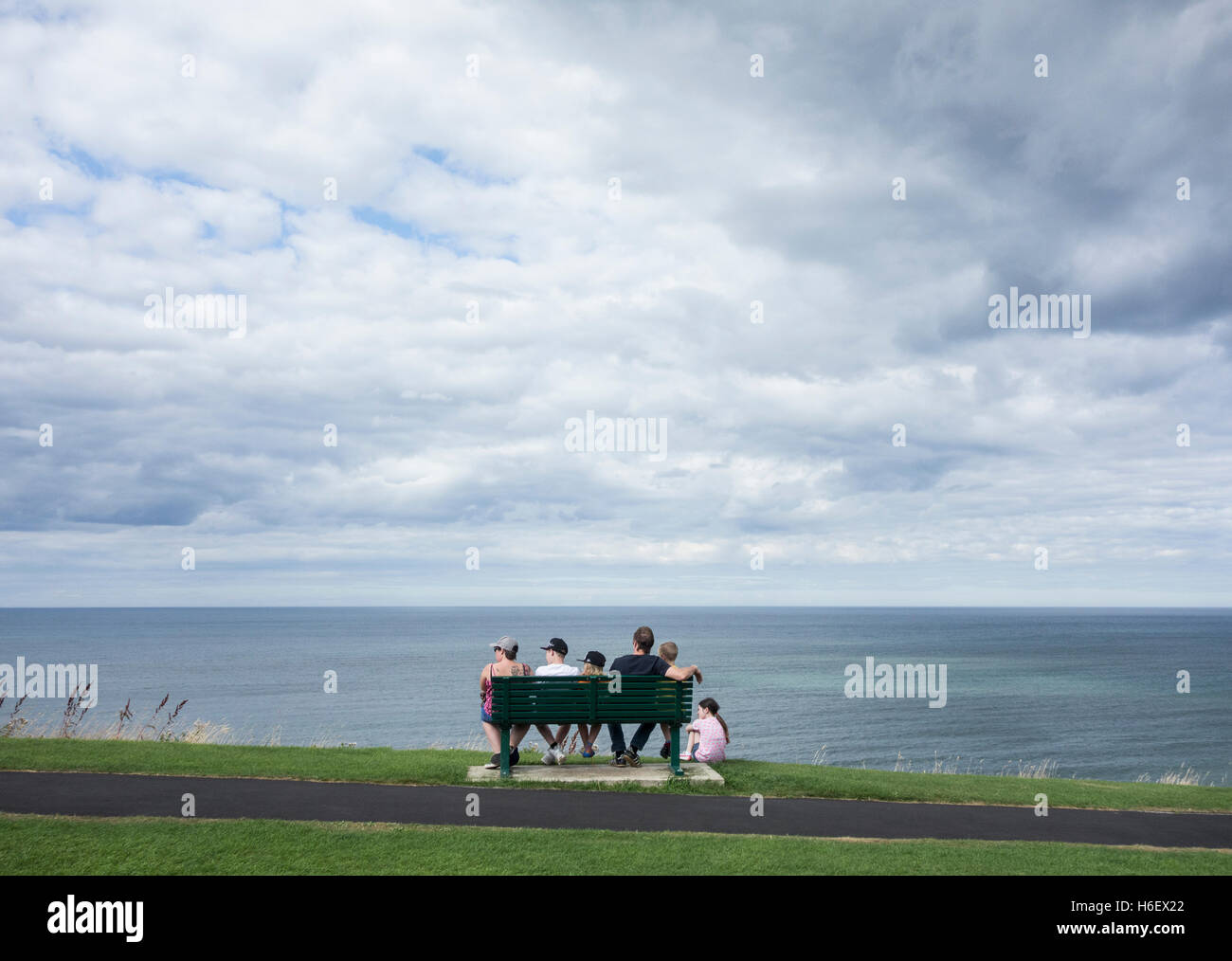 Young family of six sitting on seat overlooking the sea. Stock Photo