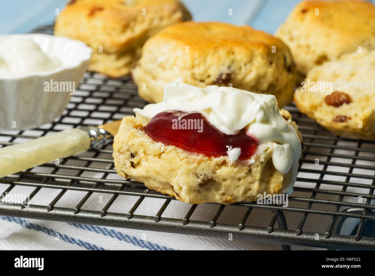 Close up of scones on cooling rack, one cut with strawberry jam and cream Stock Photo