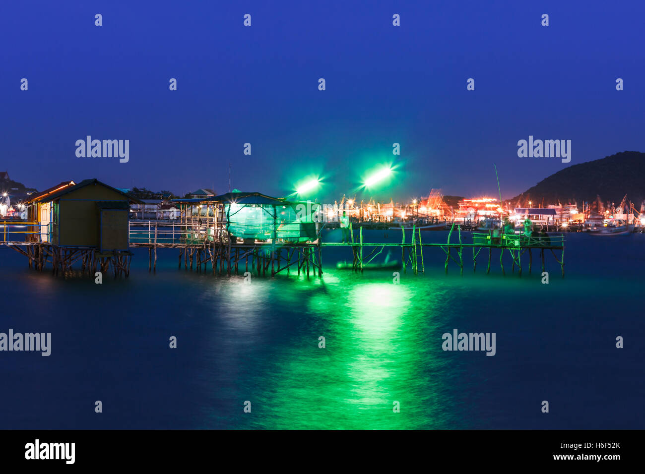 wooden house and wooden bridge on the sea at night with color light ...