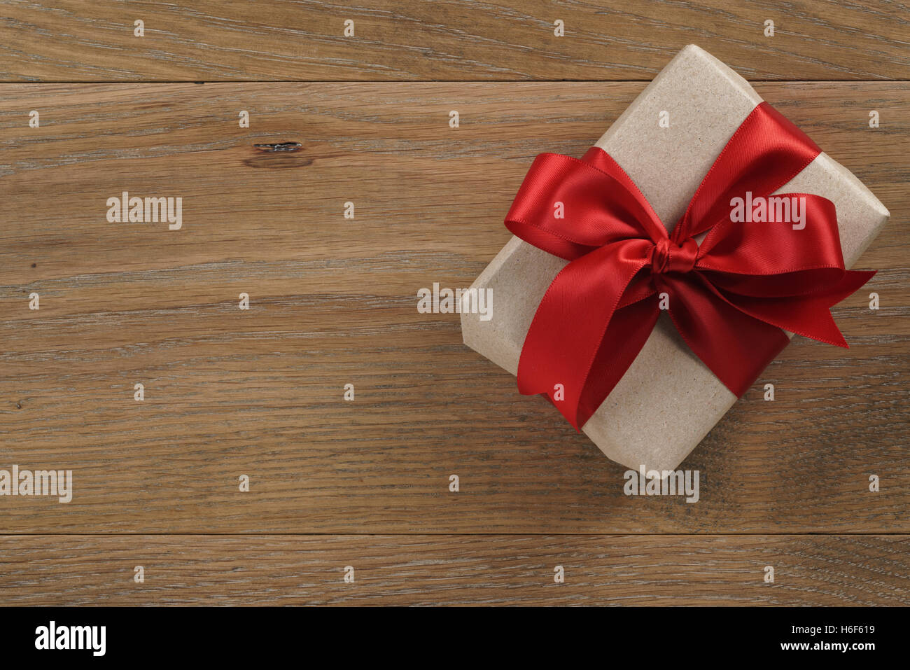 brown gift box with red ribbon bow on wooden oak table from above Stock Photo