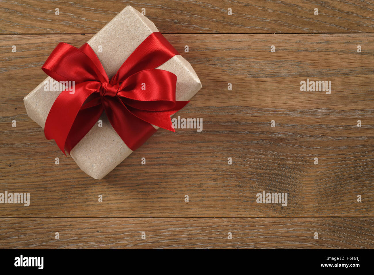 brown gift box with red ribbon bow on wooden oak table from above Stock Photo