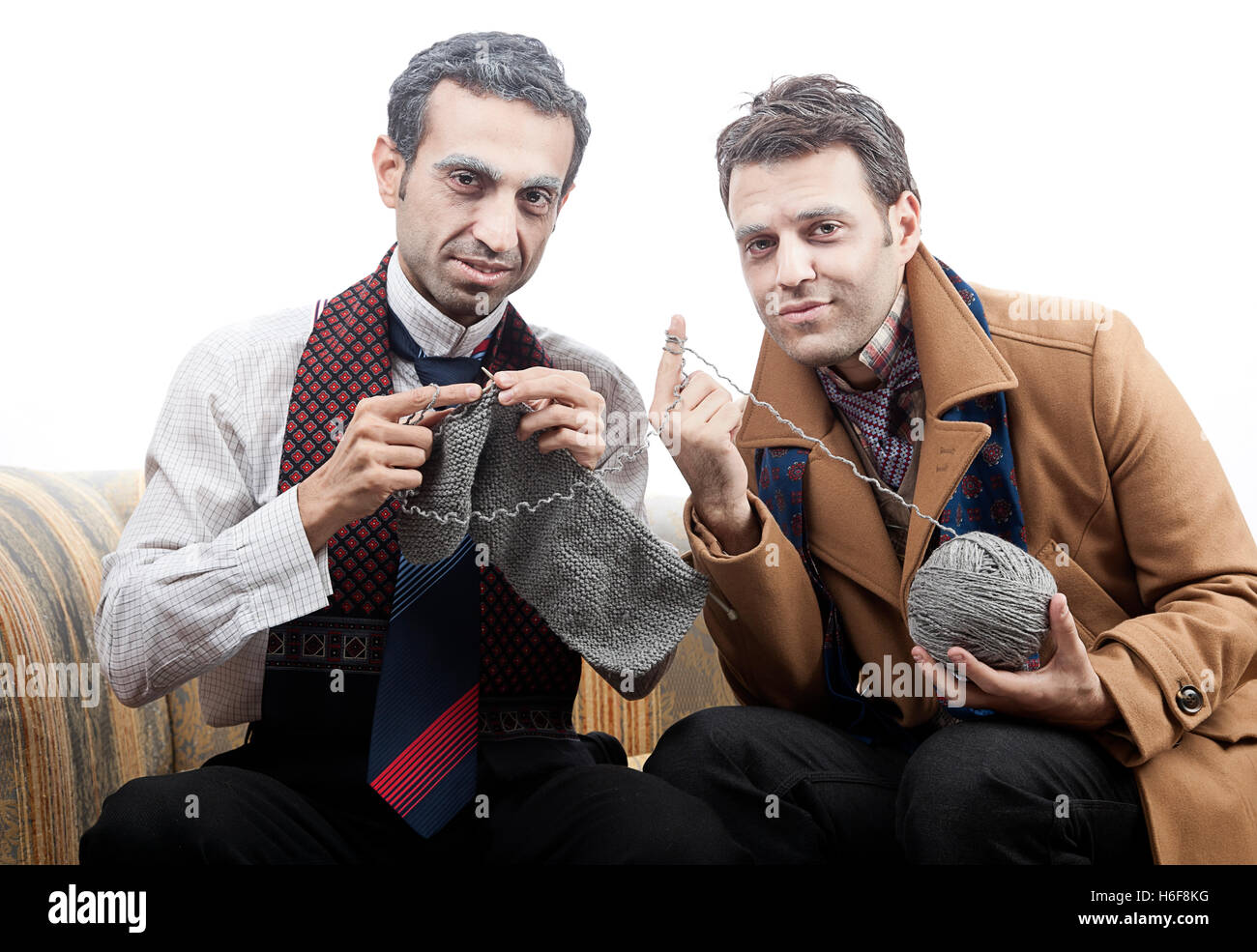 Two adult man (mid 30's and mid 20's) wearing old-man clothes and makeup, sitting on a used up vintage sofa. One of them is knit Stock Photo