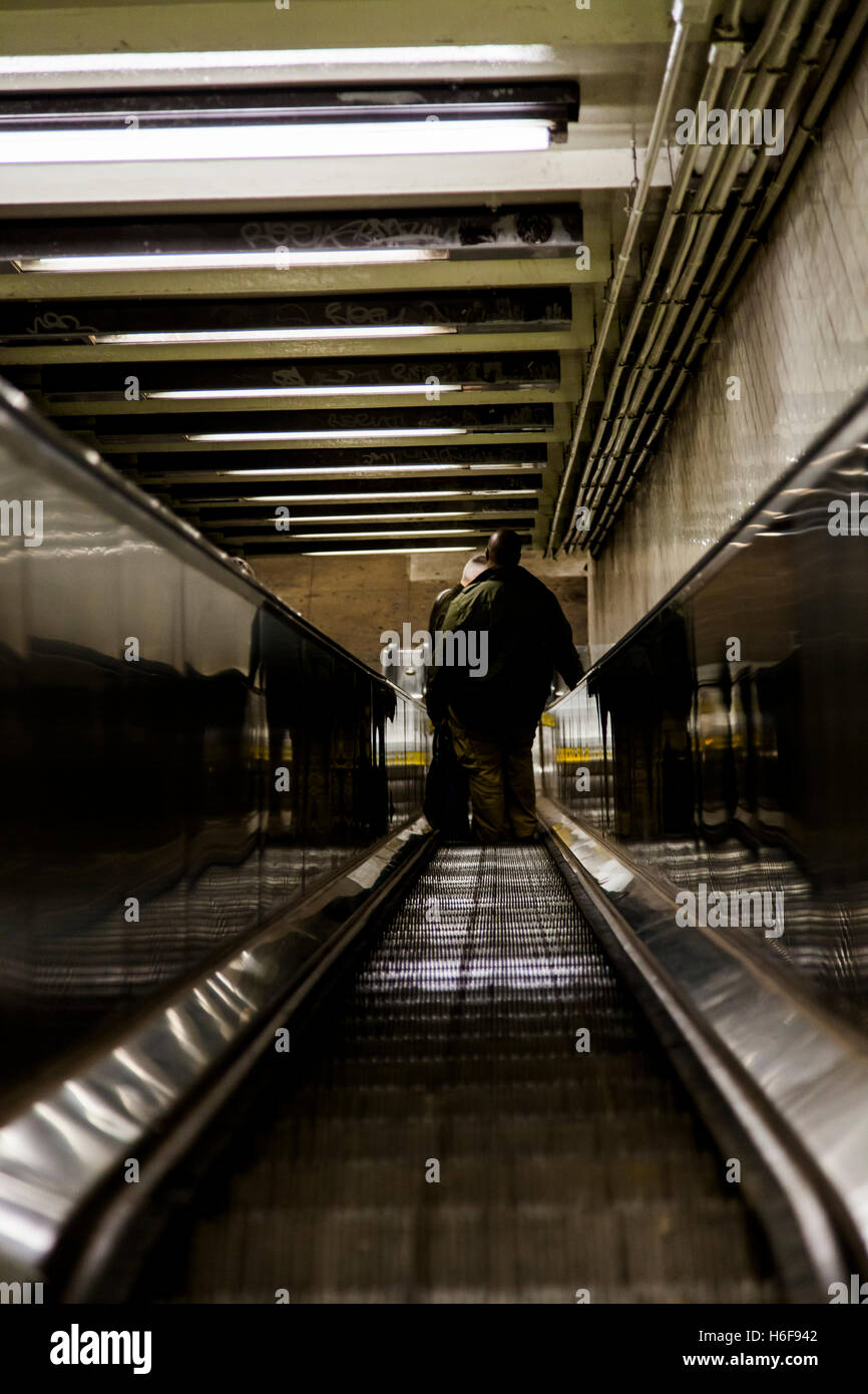 Anonymous person descending down a very long escalator connecting the street level to the subway station beneath. Stock Photo