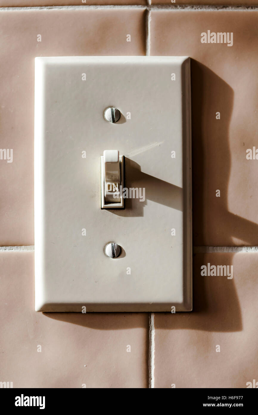 Light switch on tile ceramics wall turned on Stock Photo
