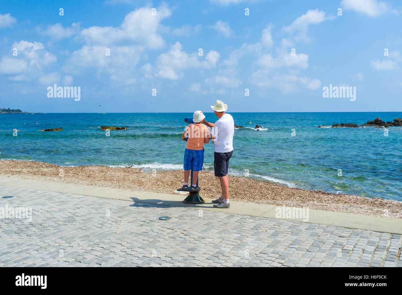 Father and son spend the time together, looking through the telescope at the coastline of Pafos, Cyprus. Stock Photo