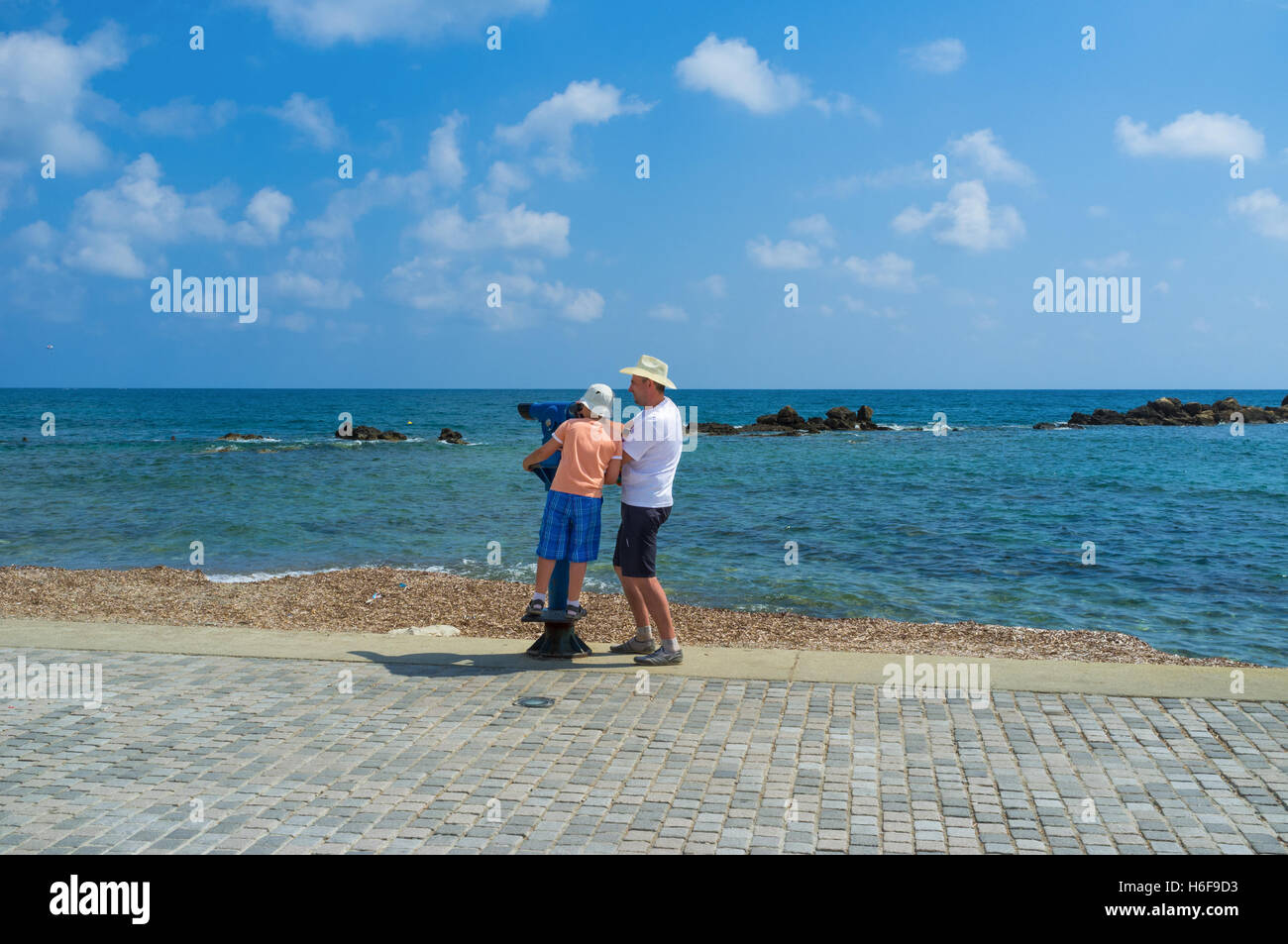 The father helps his son to look through the telescope at the coastline, Paphos. Stock Photo