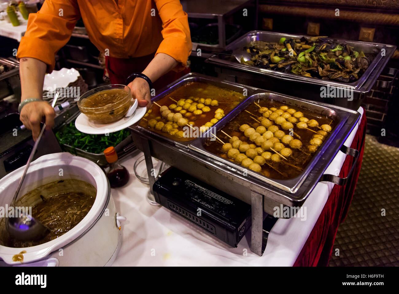 Trays full with Chinese food dishes and an anonymous worker filling a