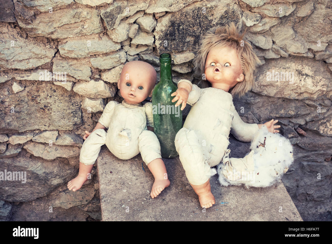 Two old dolls propped up against empty wine bottle in abandoned mountain house. Stock Photo