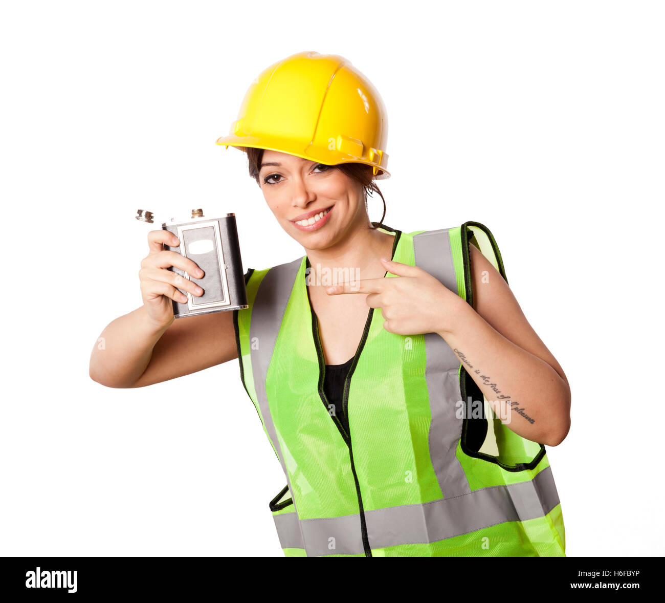 Caucasian young adult woman in her mid 20s wearing reflective yellow safety helmet and safety vest, raising a hip flask while be Stock Photo