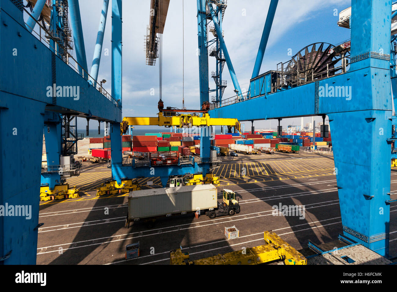 A massive freight crane transports a container from a truck onto a ...