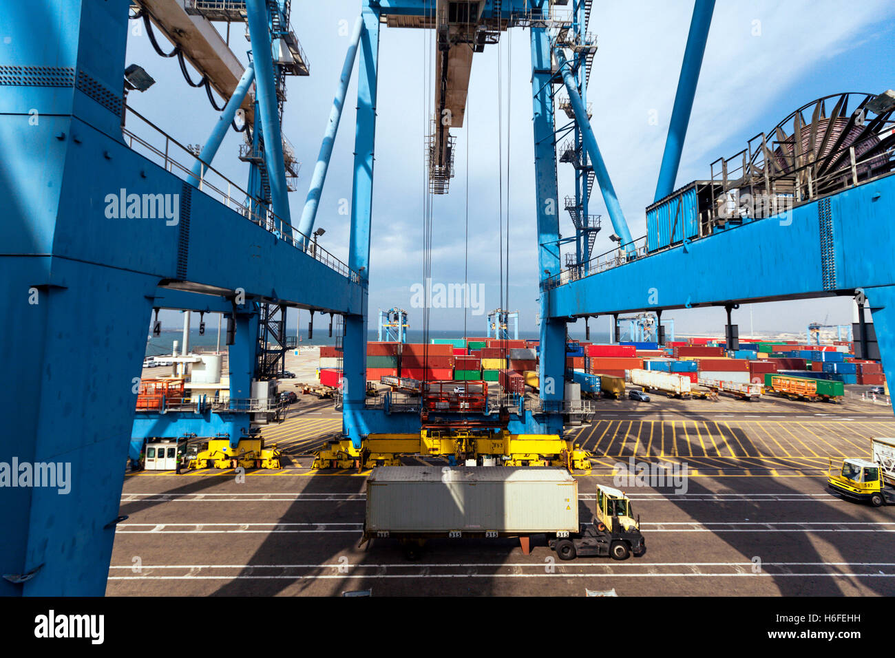 A massive freight crane transports a container from a truck onto a ...