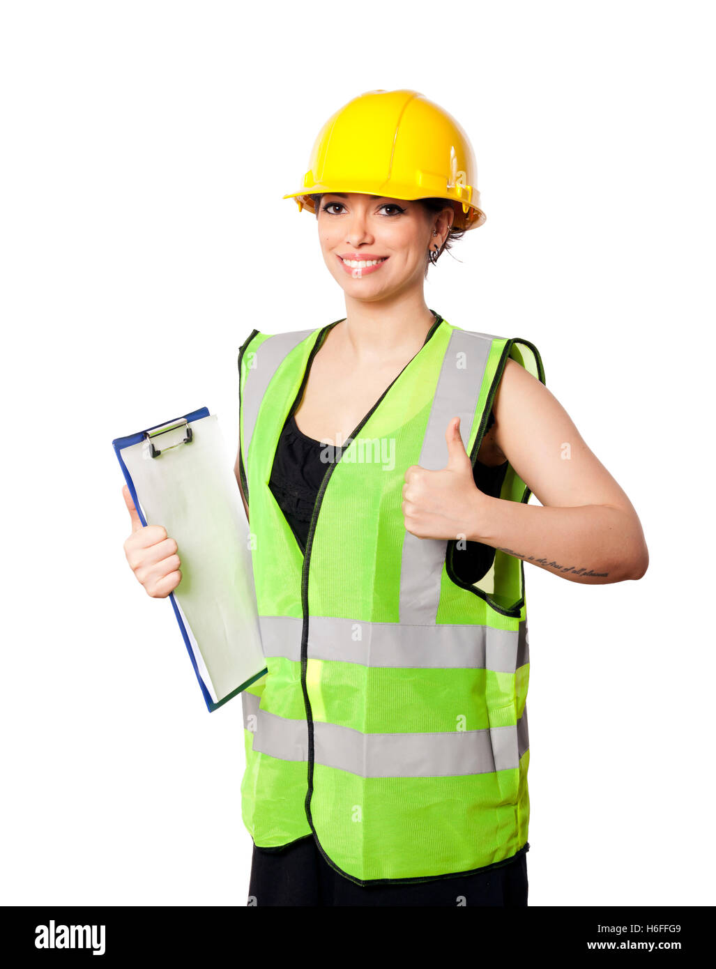 Young adult woman in her mid 20s wearing reflective yellow safety helmet and safety vest, giving the camera a smile and the thum Stock Photo