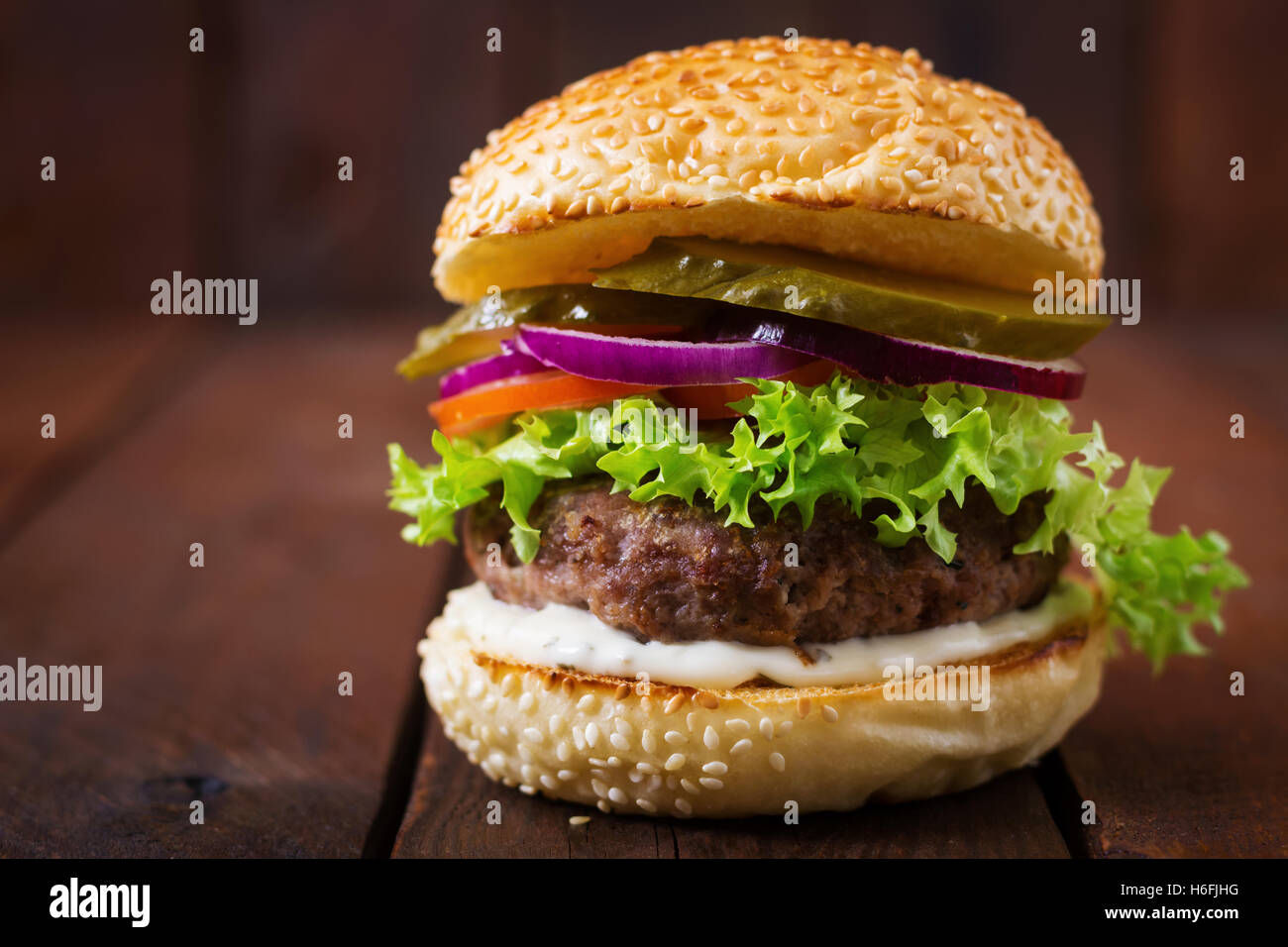 Big sandwich - hamburger burger with beef, pickles, tomato and tartar sauce on wooden background. Stock Photo