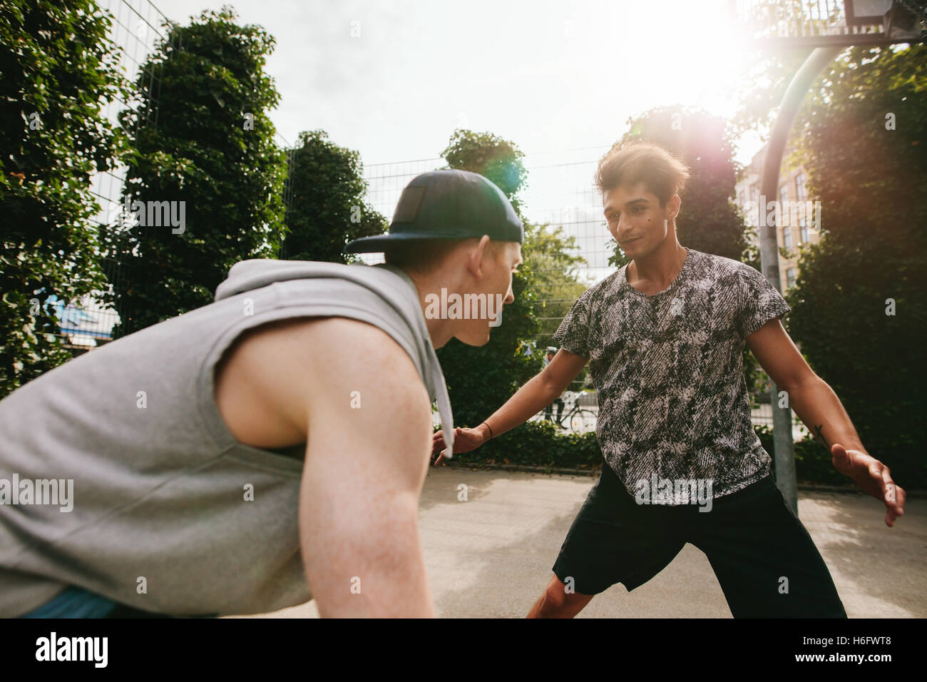 Outdoor shot of two teenage friends playing basketball. Two young men playing basketball on court outdoors. Stock Photo