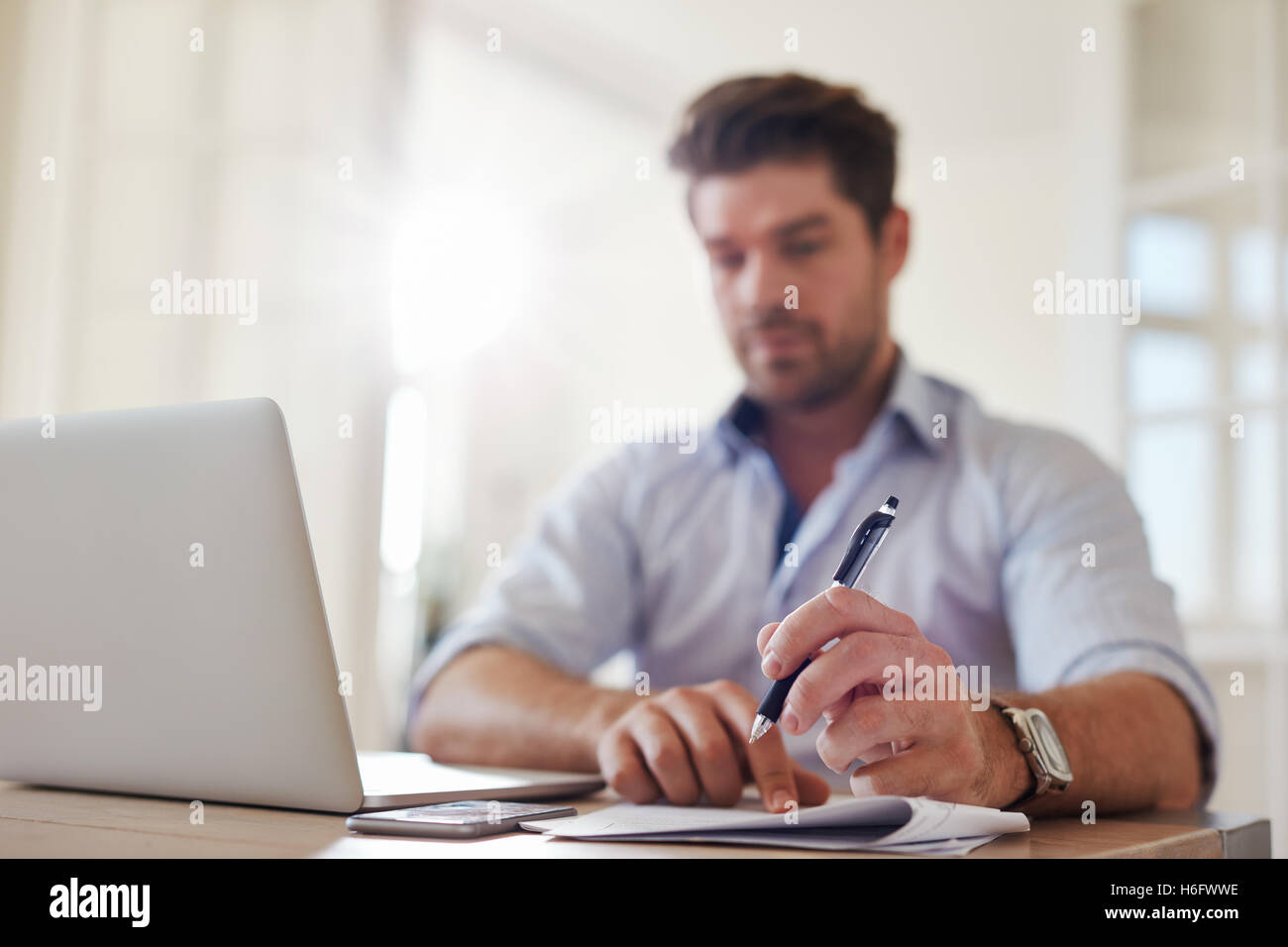 Shot of young businessman at home office with laptop and taking notes. Focus on man hands holding pen. Stock Photo