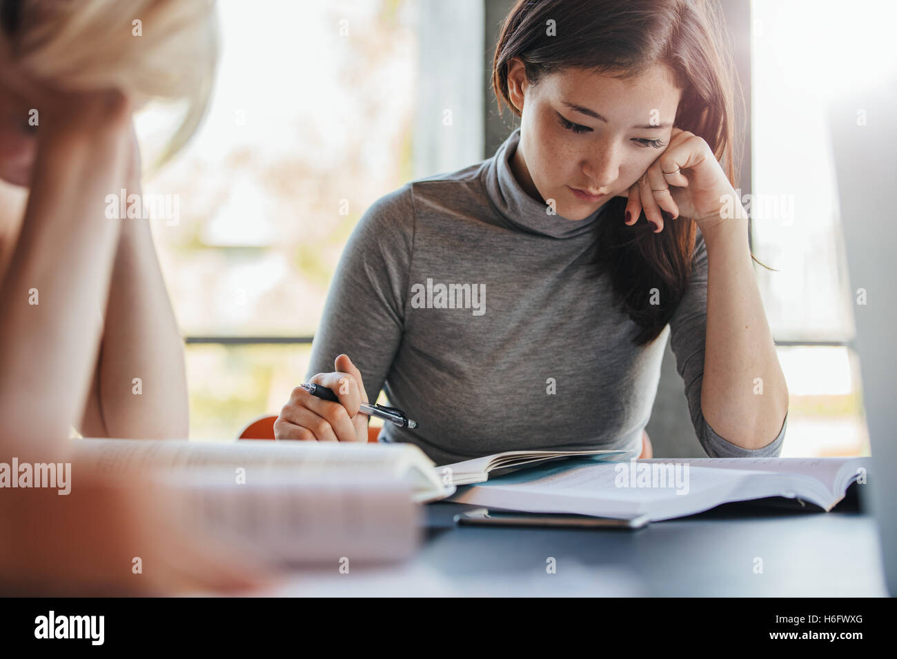 Young asian woman reading books with classmates studying around in university library. Students preparing hard for final exams. Stock Photo