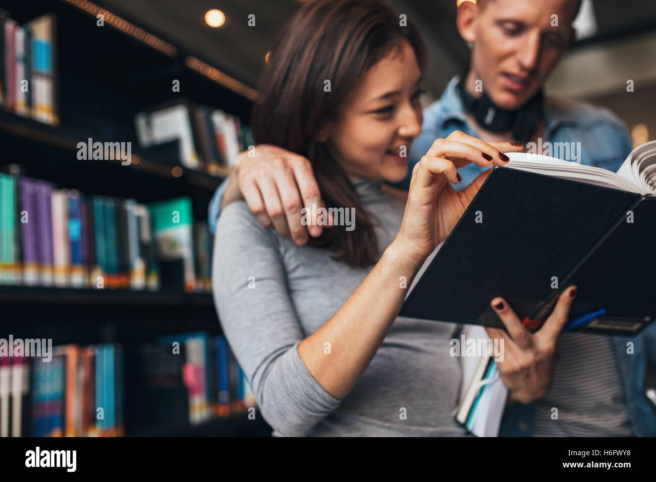 Man and woman standing by bookshelf in library reading a book. Students reading a book in a library with focus on hands. Stock Photo