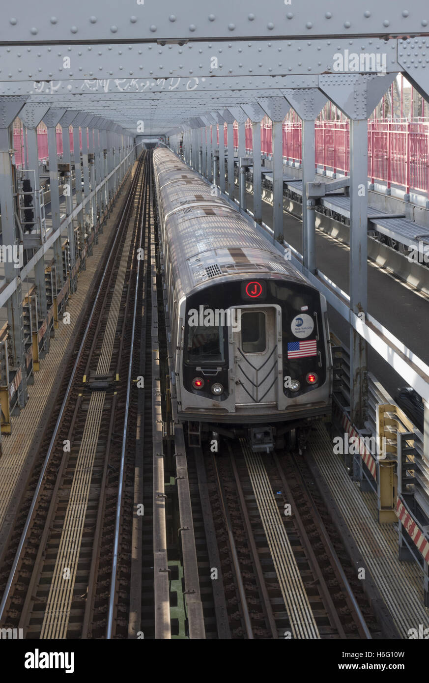 the J Train along with cars and pedestrians travels over the