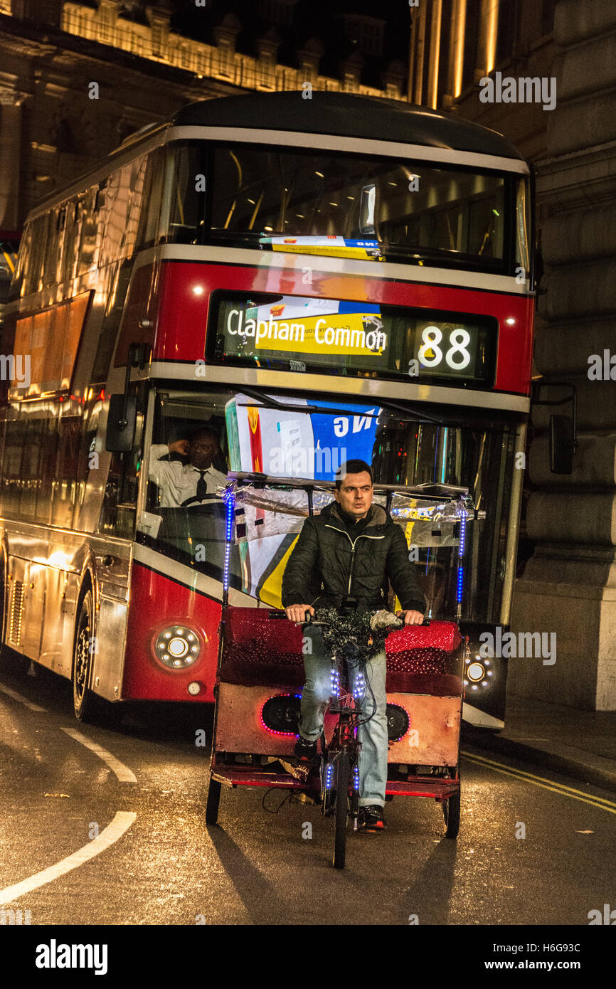 A rickshaw and driver and night-time buses pass through a brightly lit and illuminated Piccadilly Circus in central London, UK Stock Photo