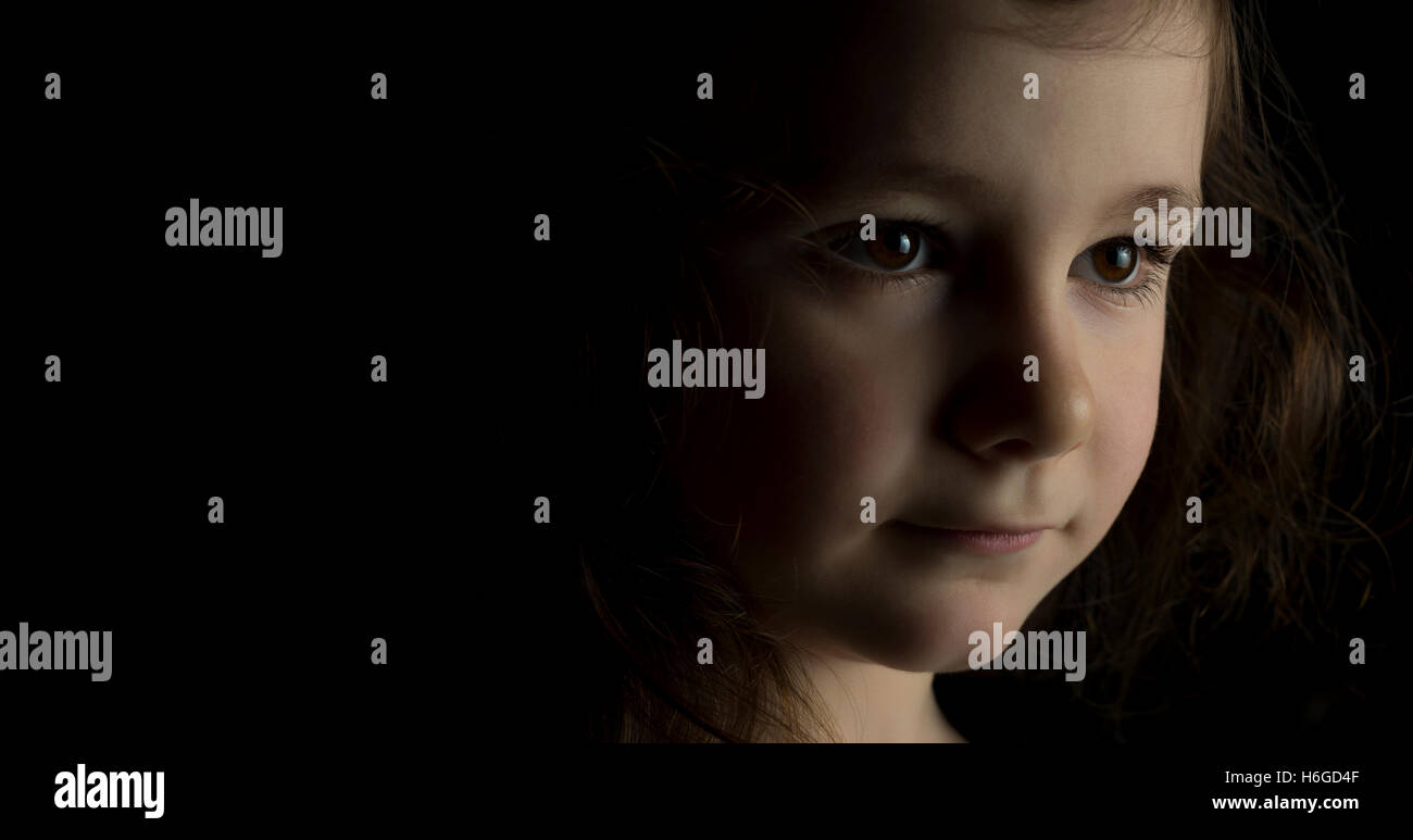 Portrait of young girl in studio on black background with copy space ...