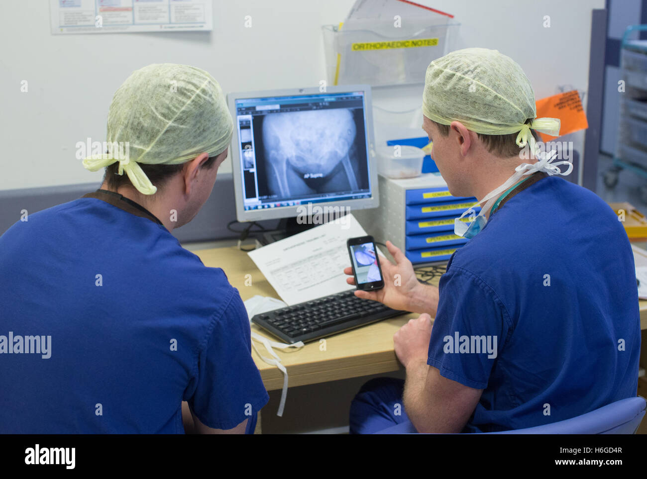 Two doctors discussing a patient X Ray on the screen showing a broken leg.They discuss images and notes on the mobile phone. Stock Photo