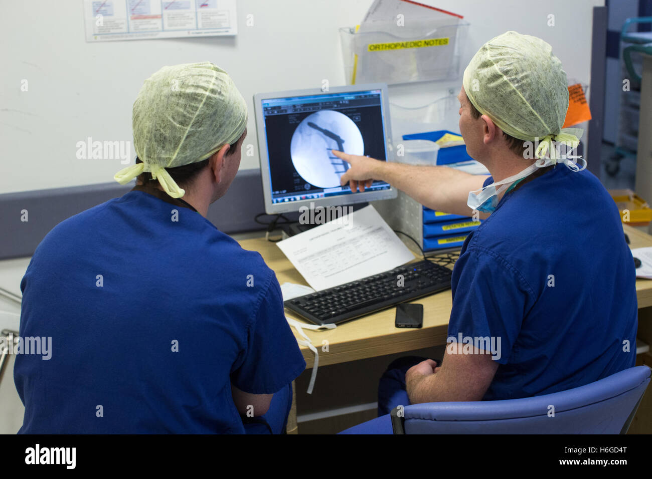 Two doctors discussing a patient X Ray on the screen showing a broken leg.They discuss images and notes on the mobile phone. Stock Photo