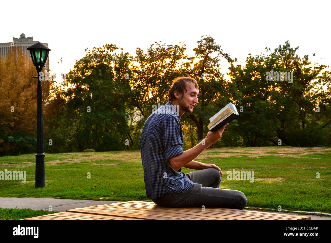 Guy sitting on a bench in the park reading book Stock Photo - Alamy