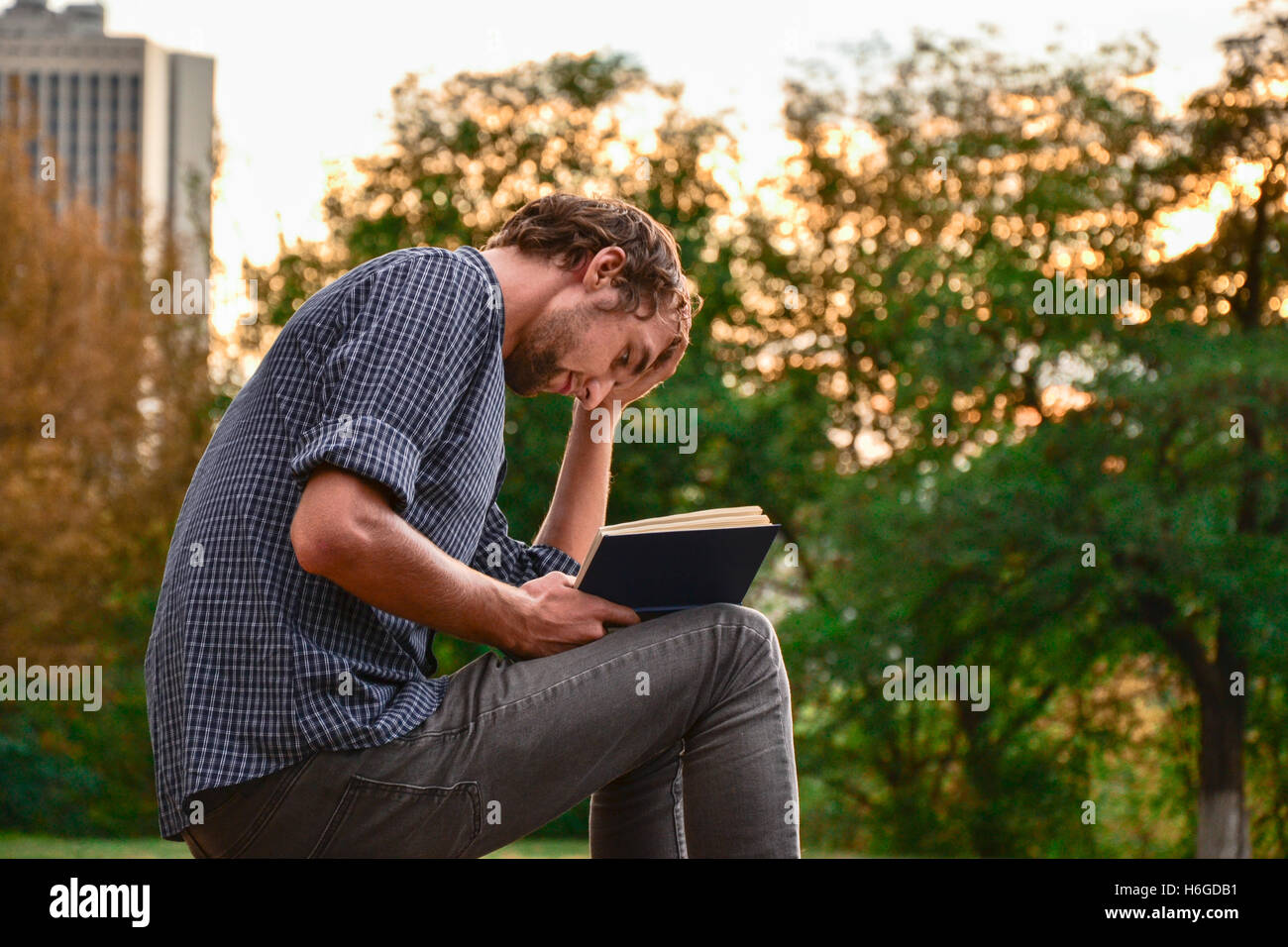 Guy sitting on a bench in the park reading book Stock Photo