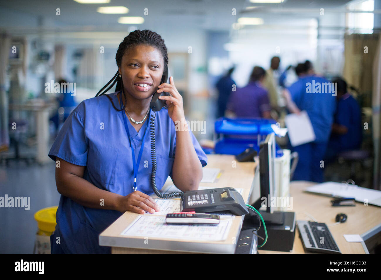 Hospital nurse at a workstation in a ward answering enquiries and checking medical records Stock Photo