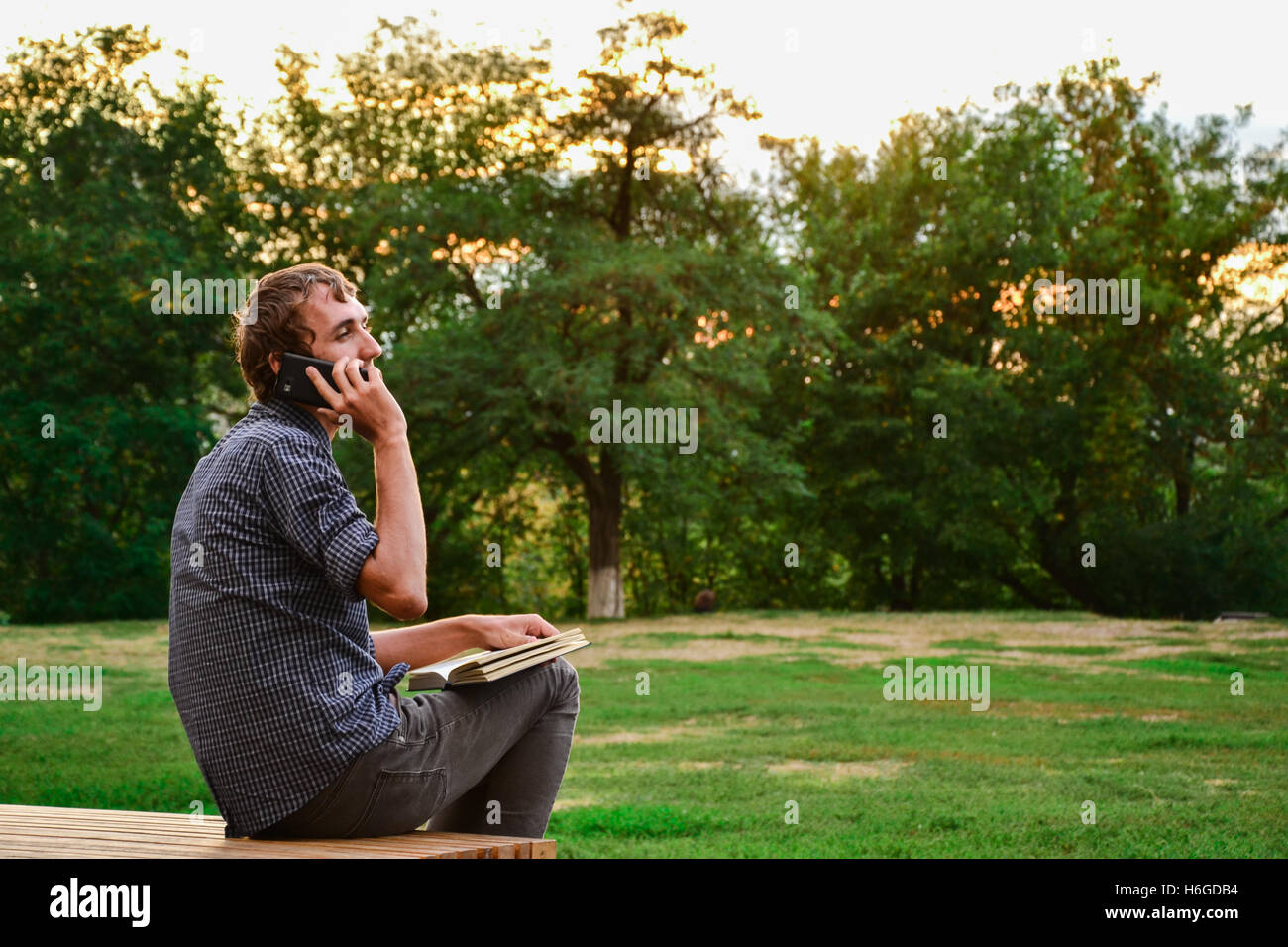 Guy with book talking on the phone in park Stock Photo