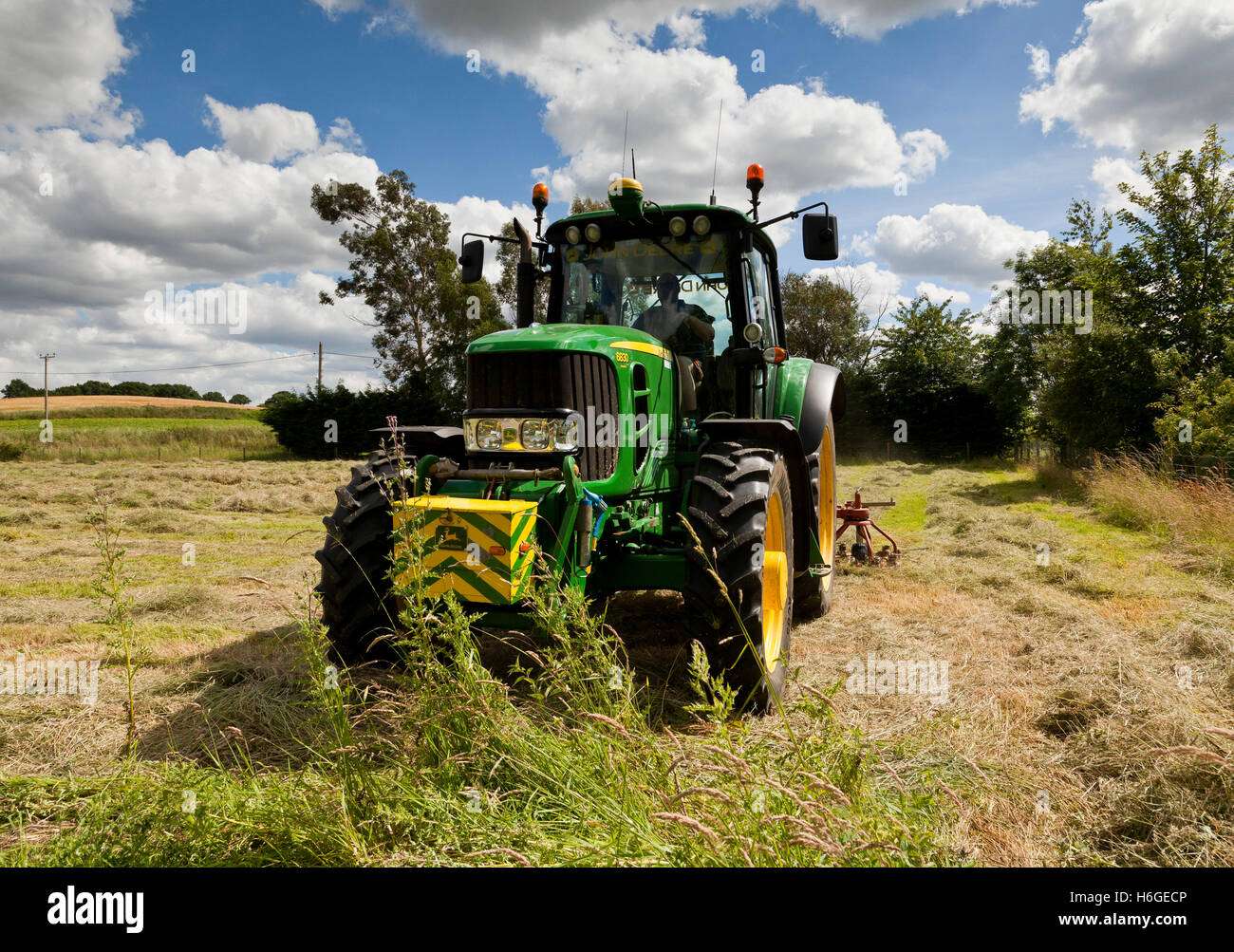 An agricultural tractor with a hay turner attached turning dried grass