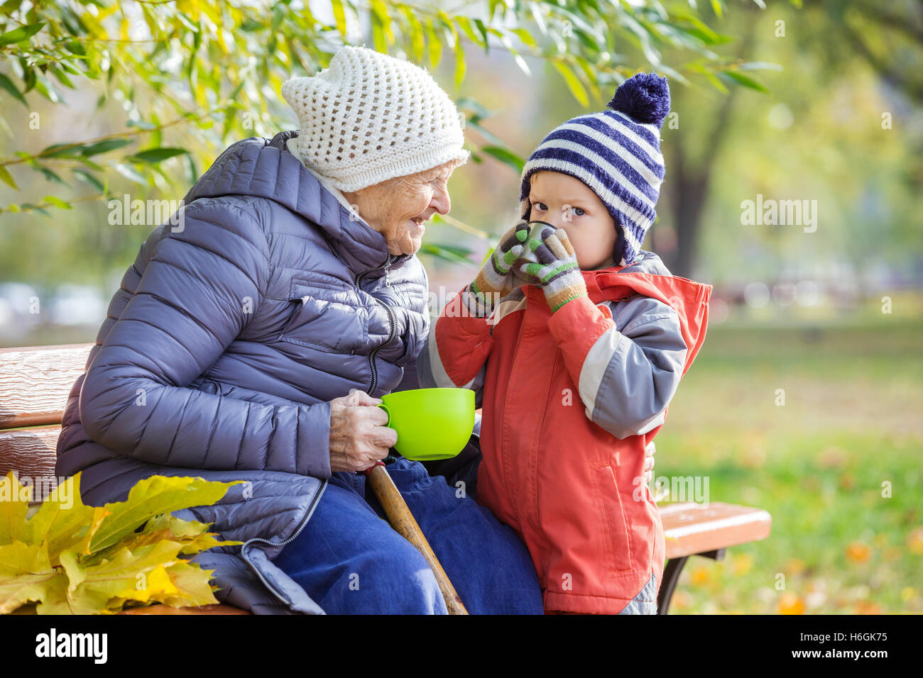 Senior woman and her great grandson drinking hot tea in autumn park Stock Photo