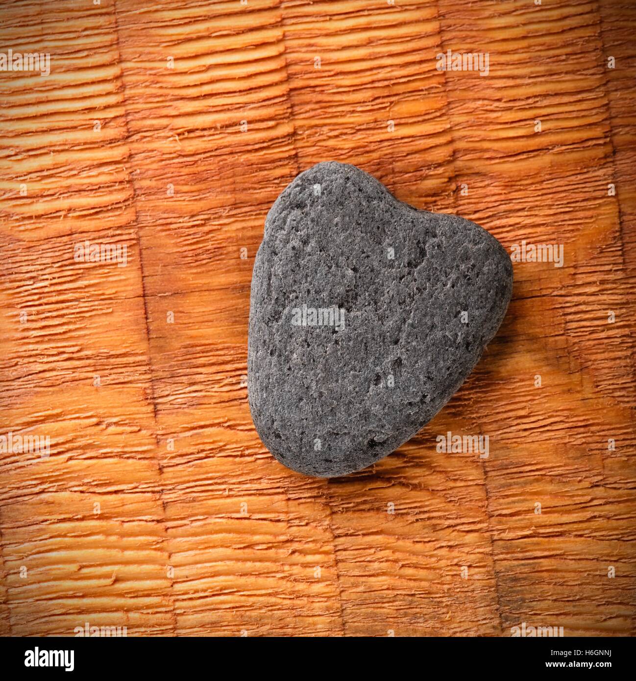 Square photo of slate grey stone with shape of heart. Heart shaped stone placed on wooden board with parallel grooves. Corners w Stock Photo