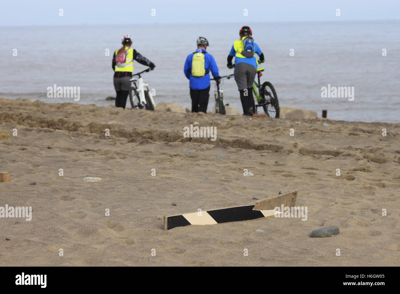 People riding bikes bicycles on beach sand coast at Spurn Point, East Yorkshire, England with road sign half buried in sand. Stock Photo