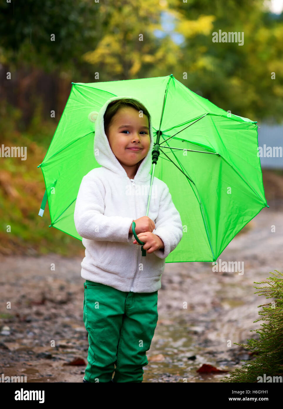 baby girl with an umbrella in the rain runs through the puddles playing on nature Stock Photo