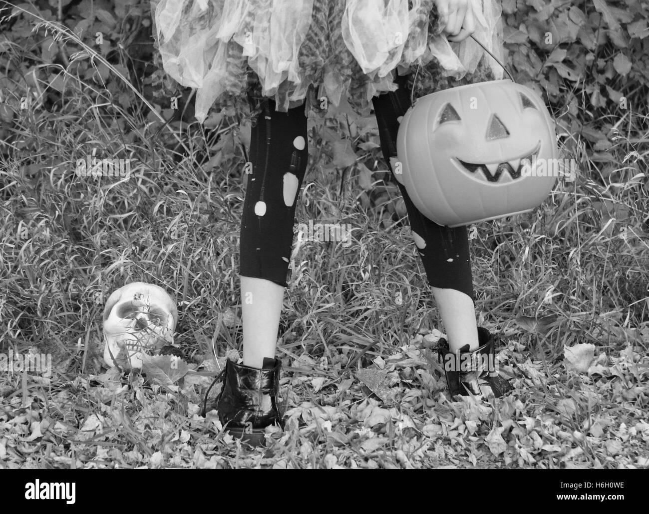 girl in tutu standing in forest with trick or treat bucket and torn clothing looking at bones or skull Stock Photo