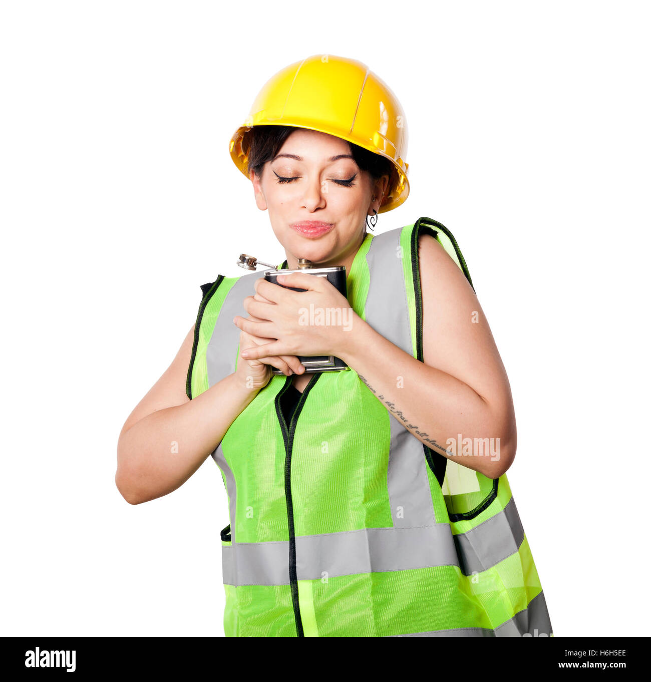 Caucasian young adult woman in her mid 20s wearing reflective yellow safety helmet and safety vest, hugging a hip flask. Isolate Stock Photo