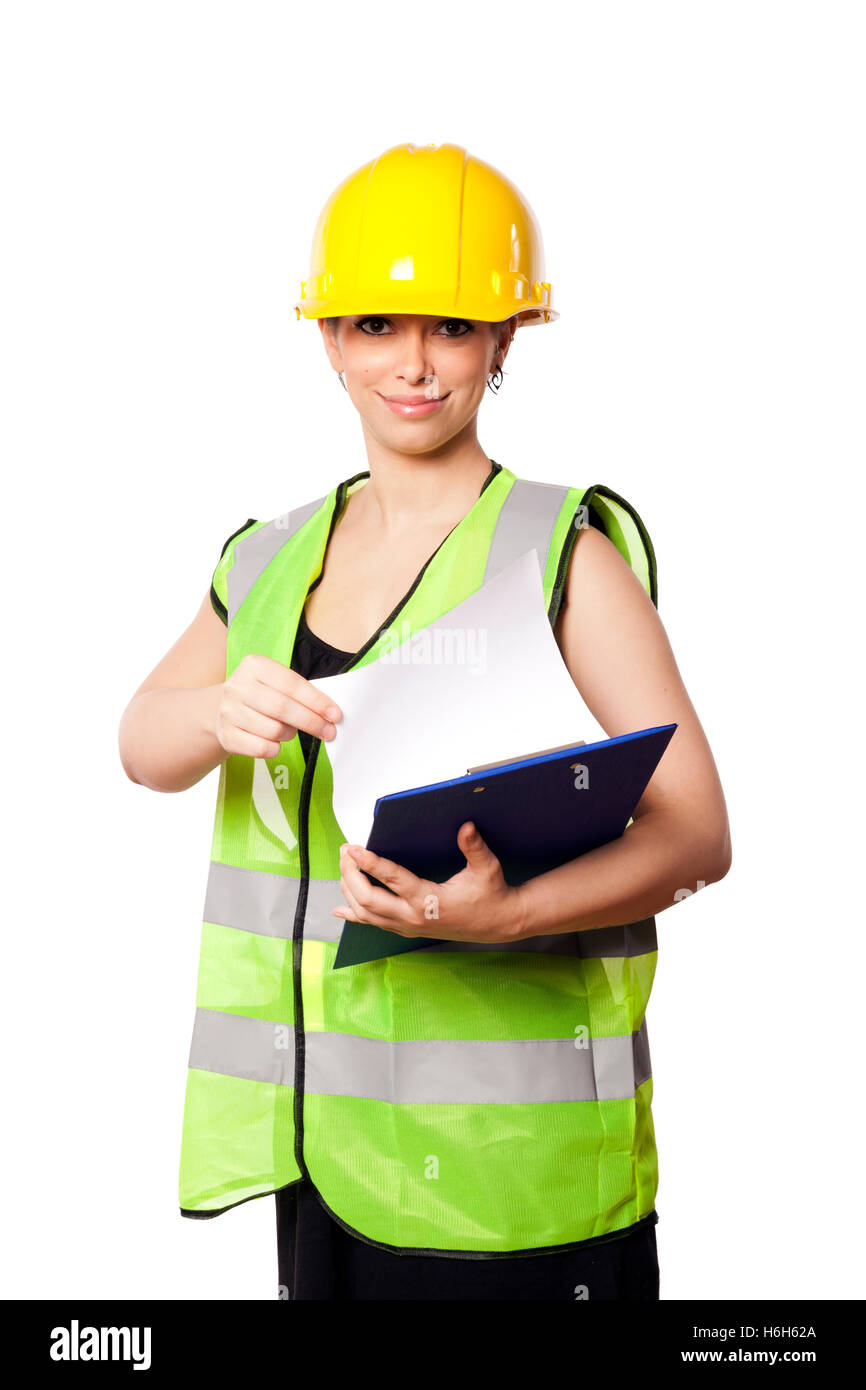 Young adult woman in her mid 20s wearing reflective yellow safety helmet and safety vest, giving the camera a smile while holdin Stock Photo