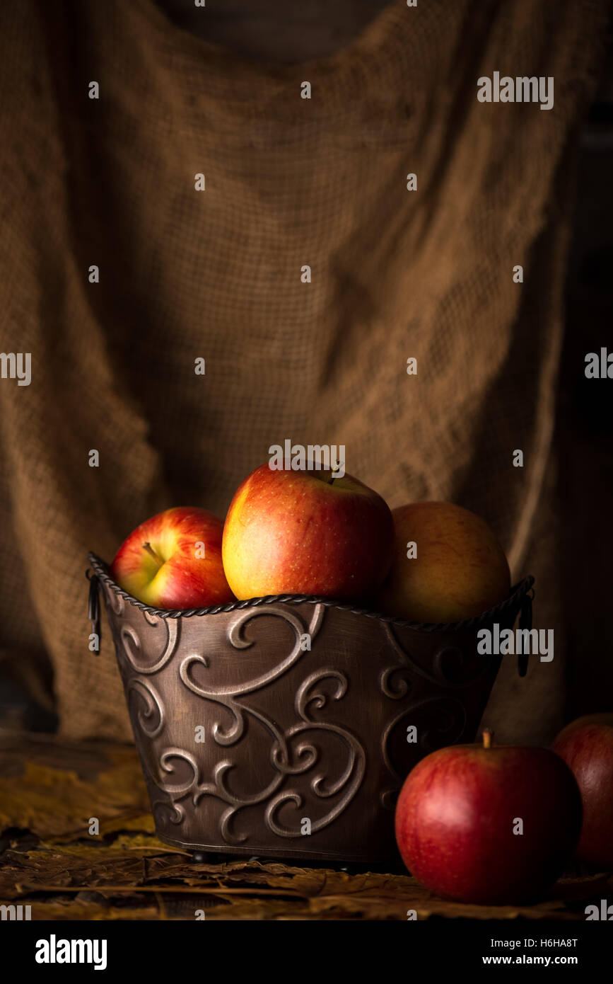 Apples in distressed metal bucket with leaf. Subdued lighting. Stock Photo