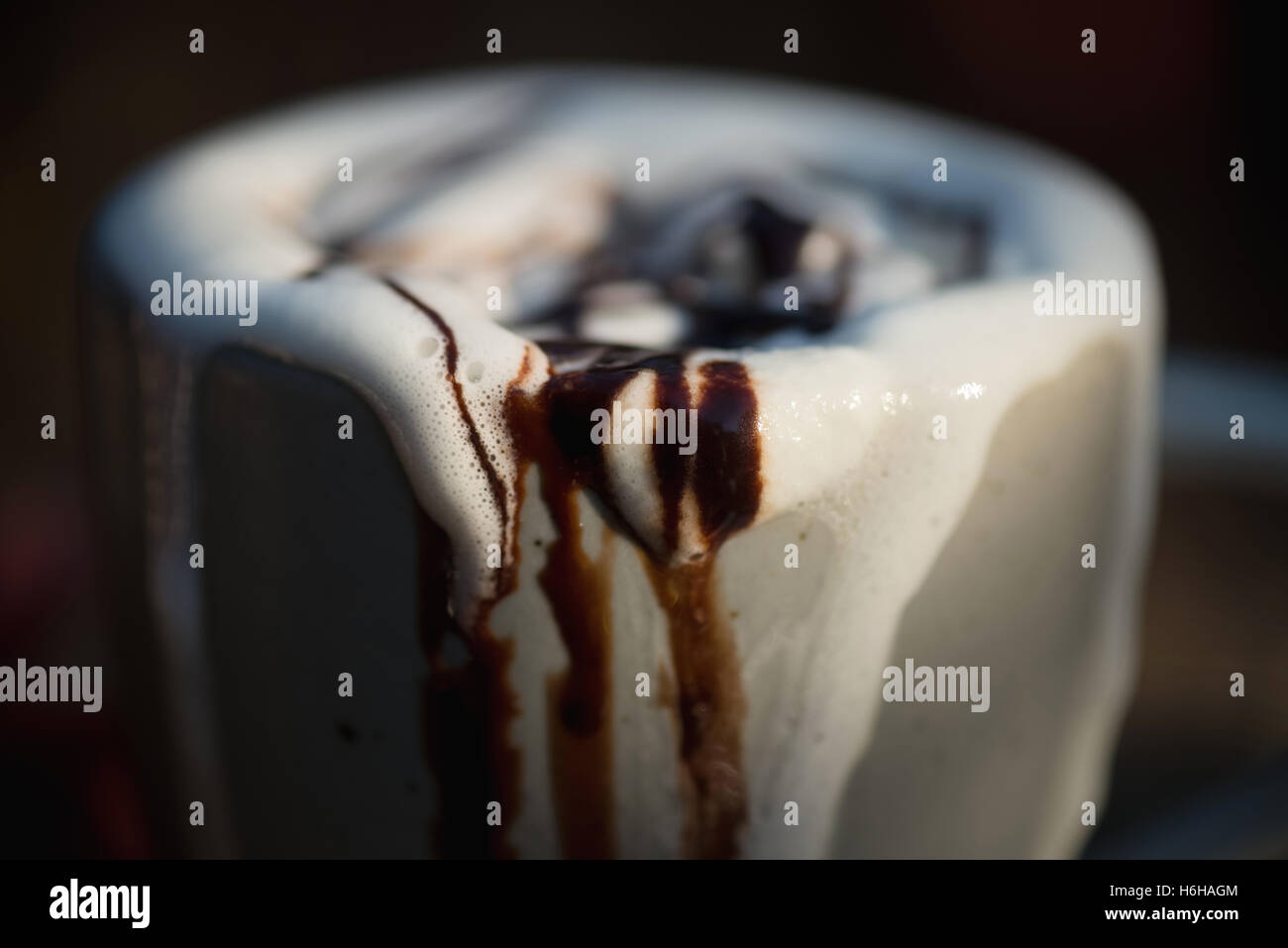 Very messy hot chocolate with whipped cream and chocolate sauce overflowing a mug set on tree stump Stock Photo