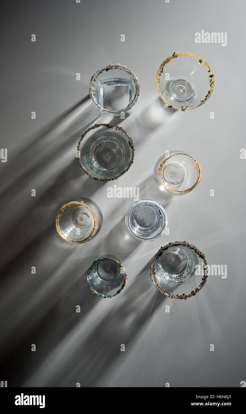 Various empty cocktail glasses arranged and  rimmed with salt, pepper, mint, sprinkles, and brown sugar with high contrast shado Stock Photo