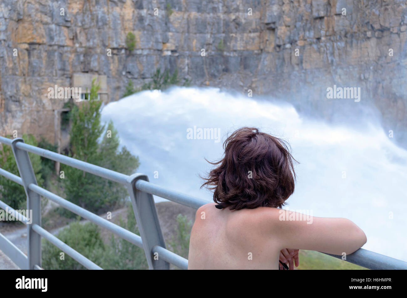 Woman looking at the water flowing through the spilway of Hydroelectric dam. Water falling strongly. Cloudy day. Stock Photo