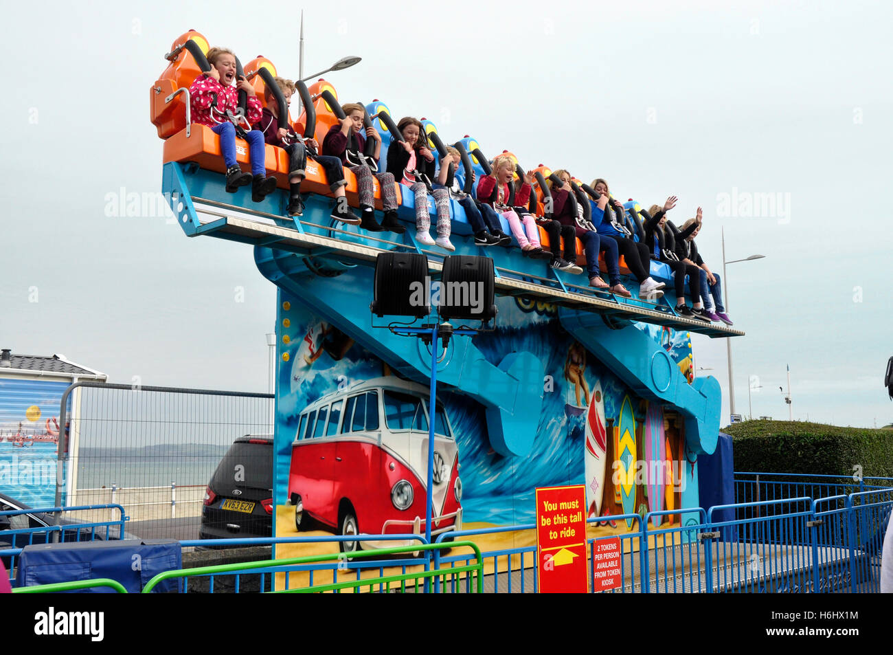 Sea front fairground -  children on a scary sky ride  - excited faces - waving hands - sunlight blue sky - Weymouth Dorset Stock Photo