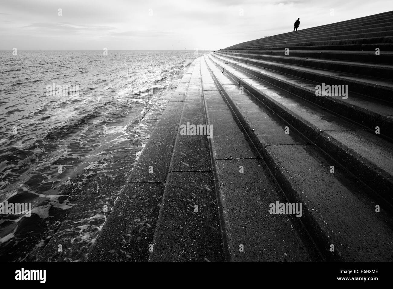 Woman walking along the top of the seawall at Heacham on the Norfolk coast. Stock Photo
