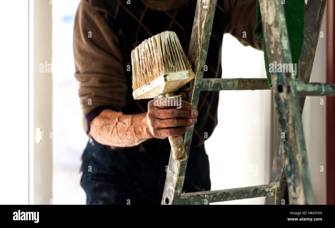 Painter on a ladder holding wall painting brush in his hand. Stock Photo