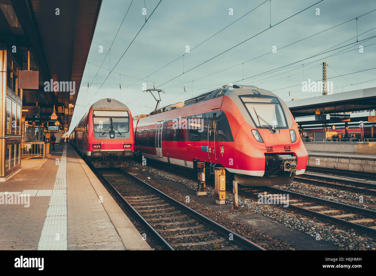 High speed red commuter trains at the railway platform. Beautiful railway station with modern  trains in the evening. Railroad w Stock Photo